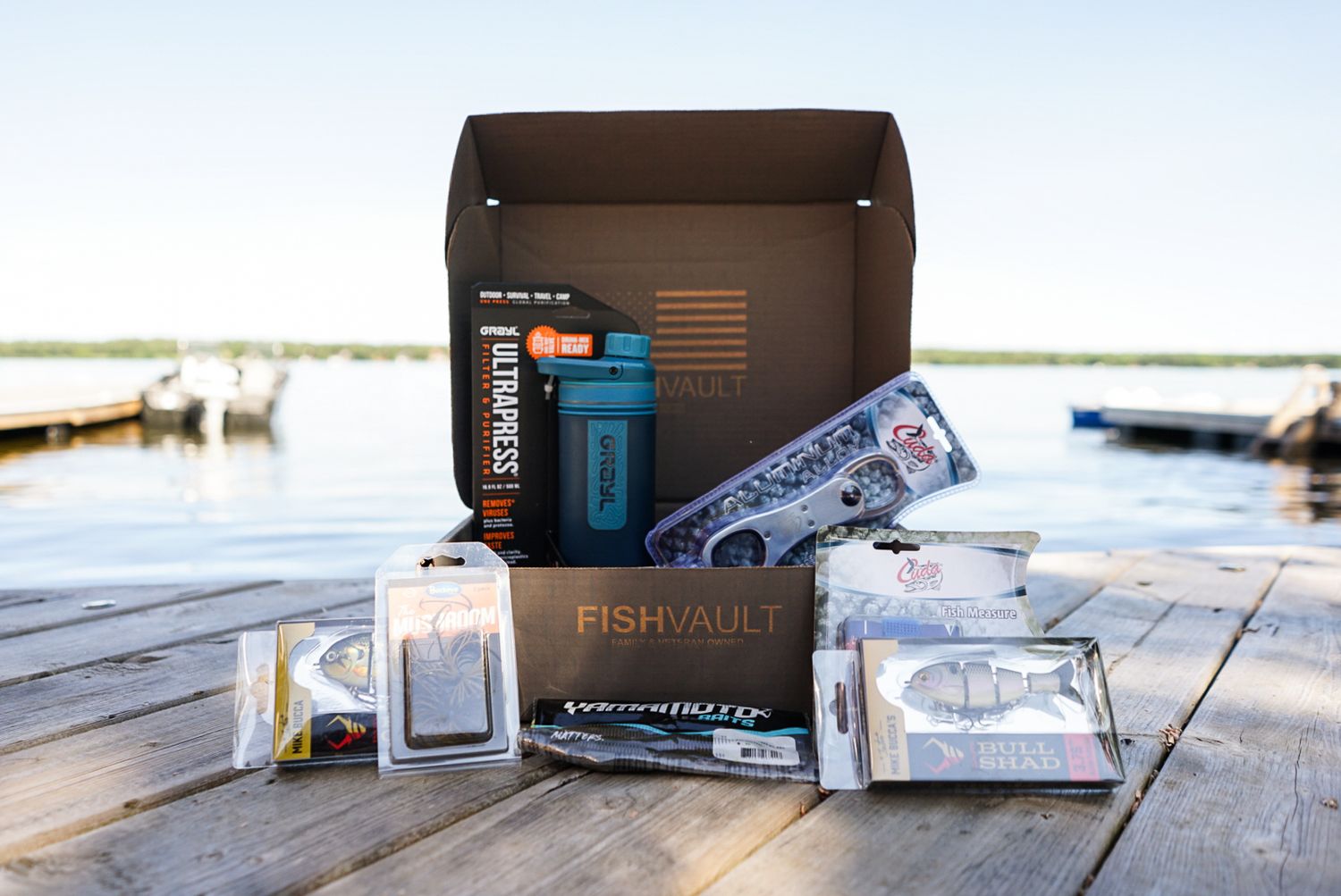 Collection of outdoor gear and equipment laid out on wooden dock by the water.