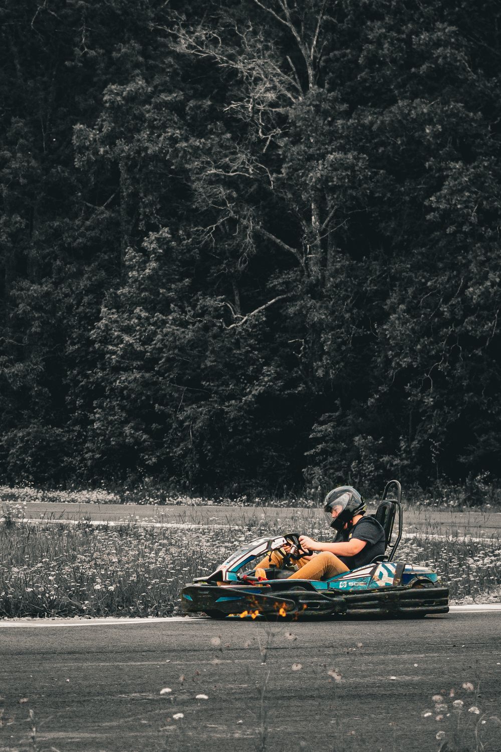Go-kart racer in orange vehicle speeding along track with forest backdrop.