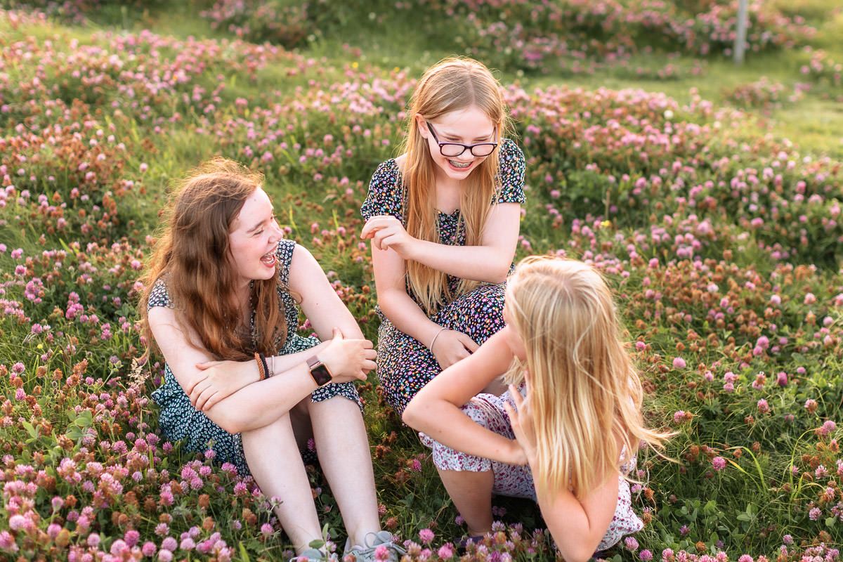 Tre søstre som sitter i en blomstereng og ler.