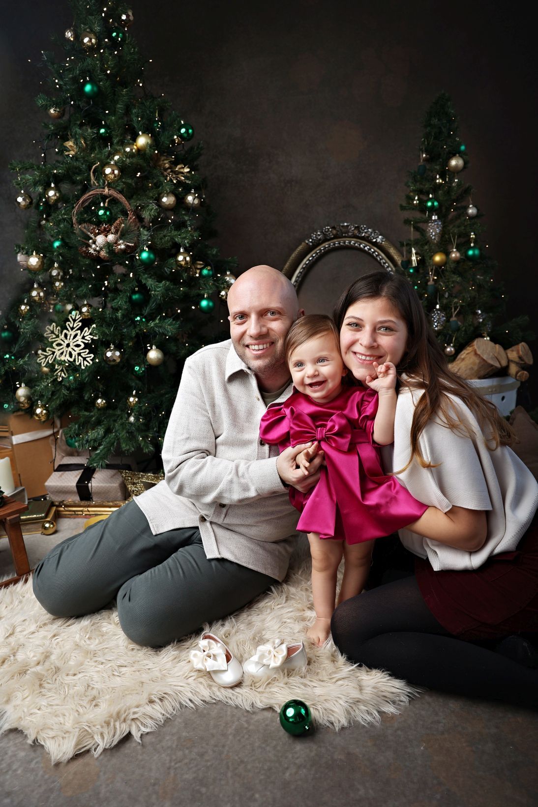 Holiday family portrait with decorated Christmas trees and cozy decor on white fur rug.