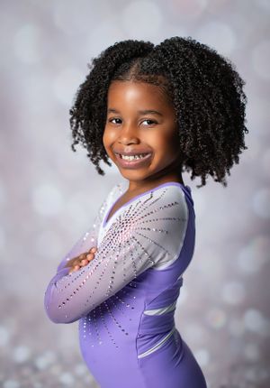Athletic portrait in purple sparkly gymnastics leotard against sparkly backdrop.