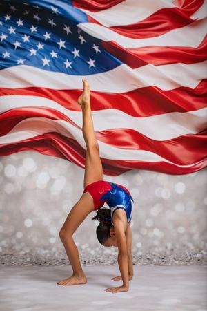 Gymnast performs backbend against American flag backdrop with sparkling bokeh effect.