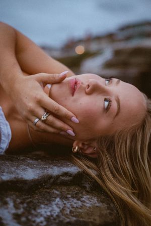 Person reclining on coastal rocks with serene expression and blonde hair.