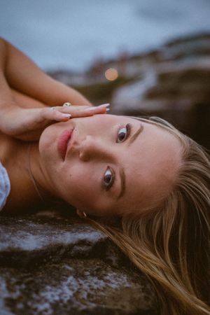 Artistic portrait of someone lying on rocky shore with gentle waves in background.