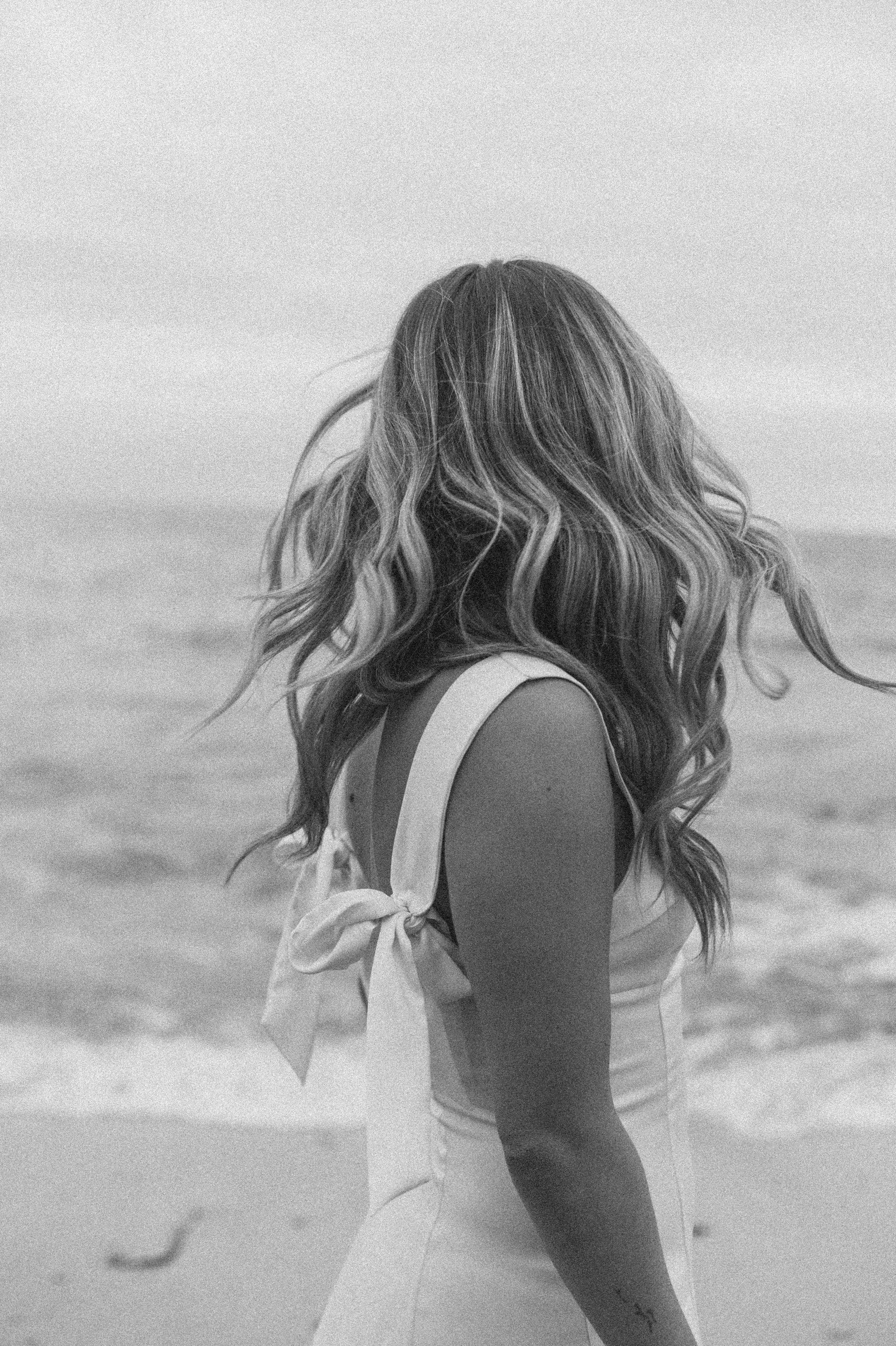Black and white portrait of someone in a white dress by the ocean.