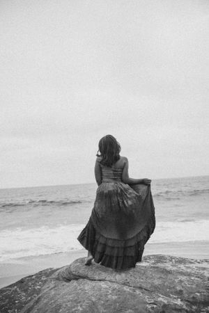 Silhouette of a figure in a flowing dress standing on coastal rocks overlooking the ocean.