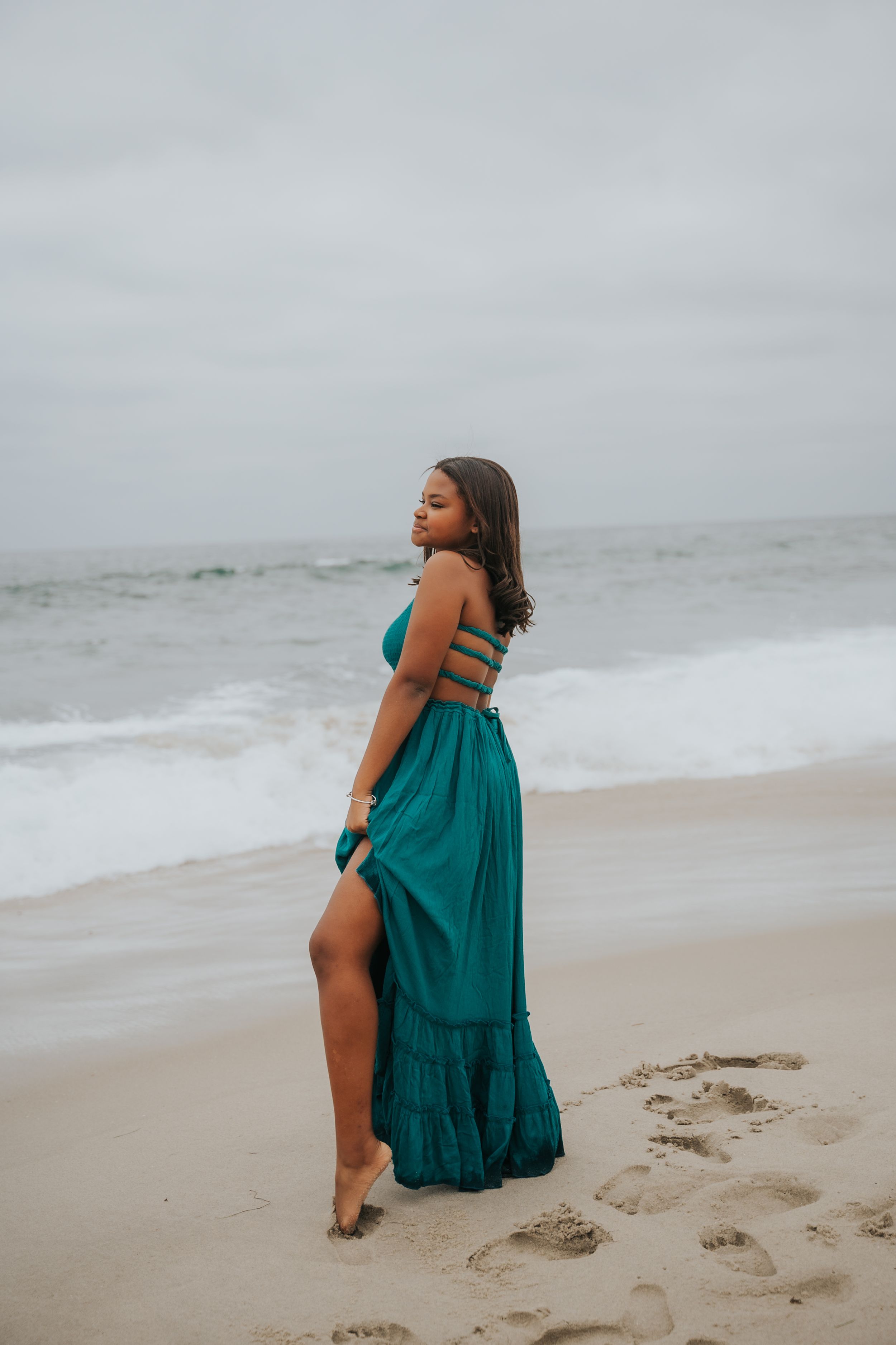 Person in turquoise dress posing gracefully on sandy beach.