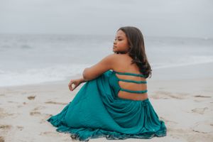 Someone in flowing turquoise dress moving expressively along shoreline.