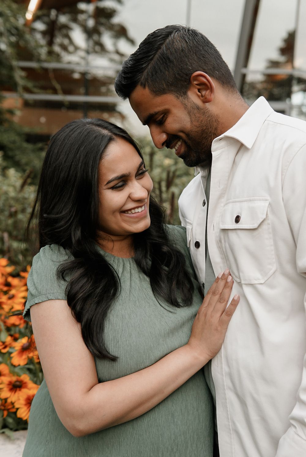 An expecting couple laughing together among late-summer flowers