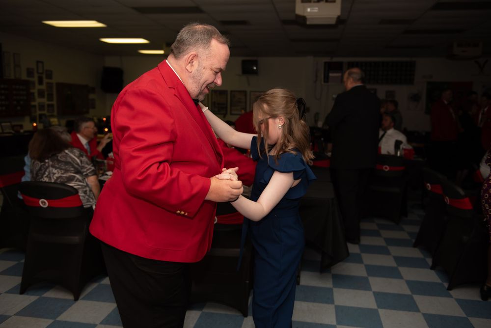 People dancing together at an indoor social event with checkered floor.