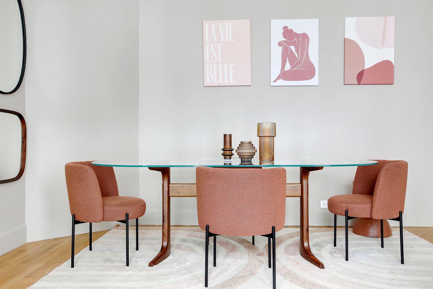 Modern dining room with glass table, terracotta chairs, and pink abstract wall art prints.
