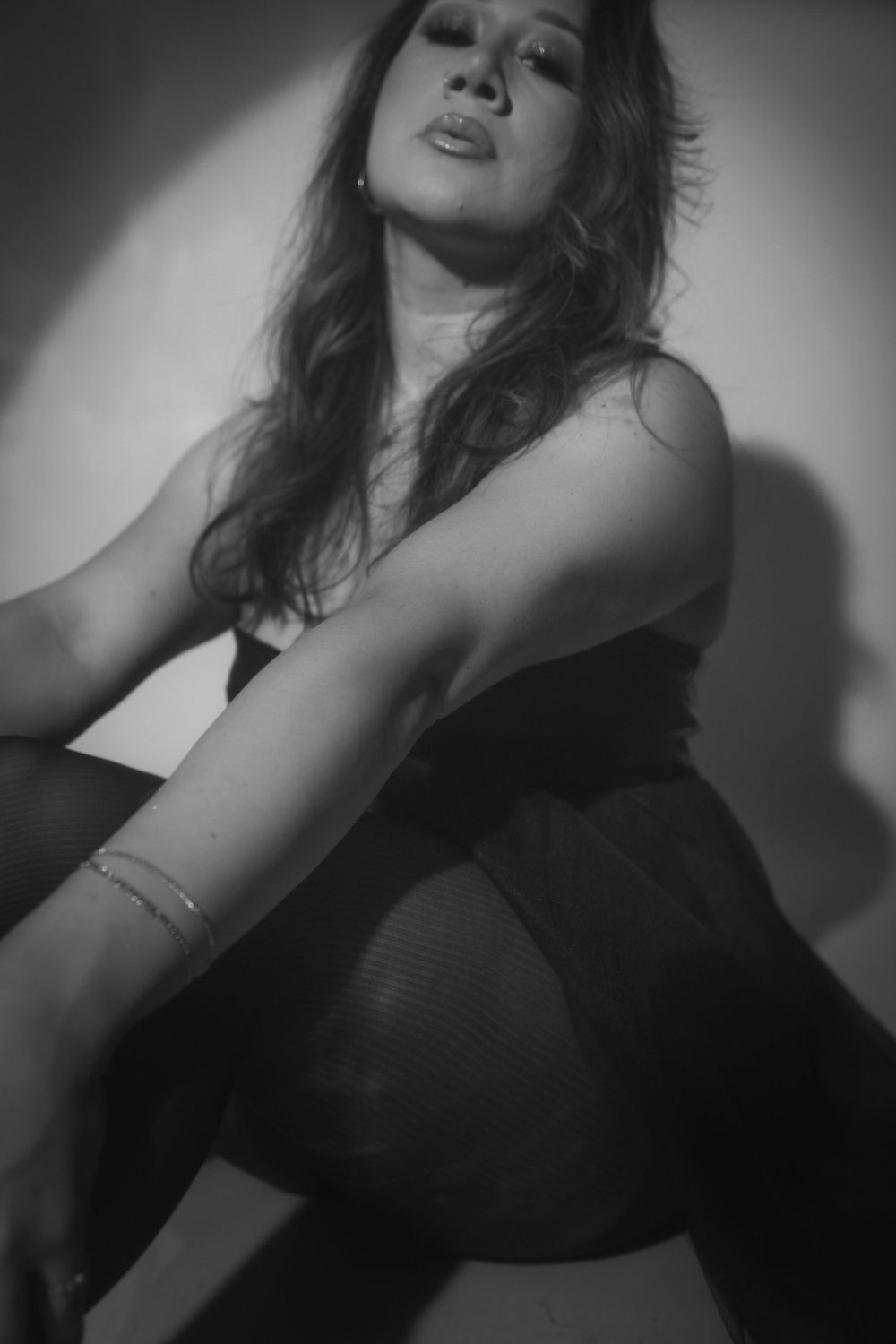 Artistic black and white portrait showcasing dramatic shadows and elegant pose against light backdrop.