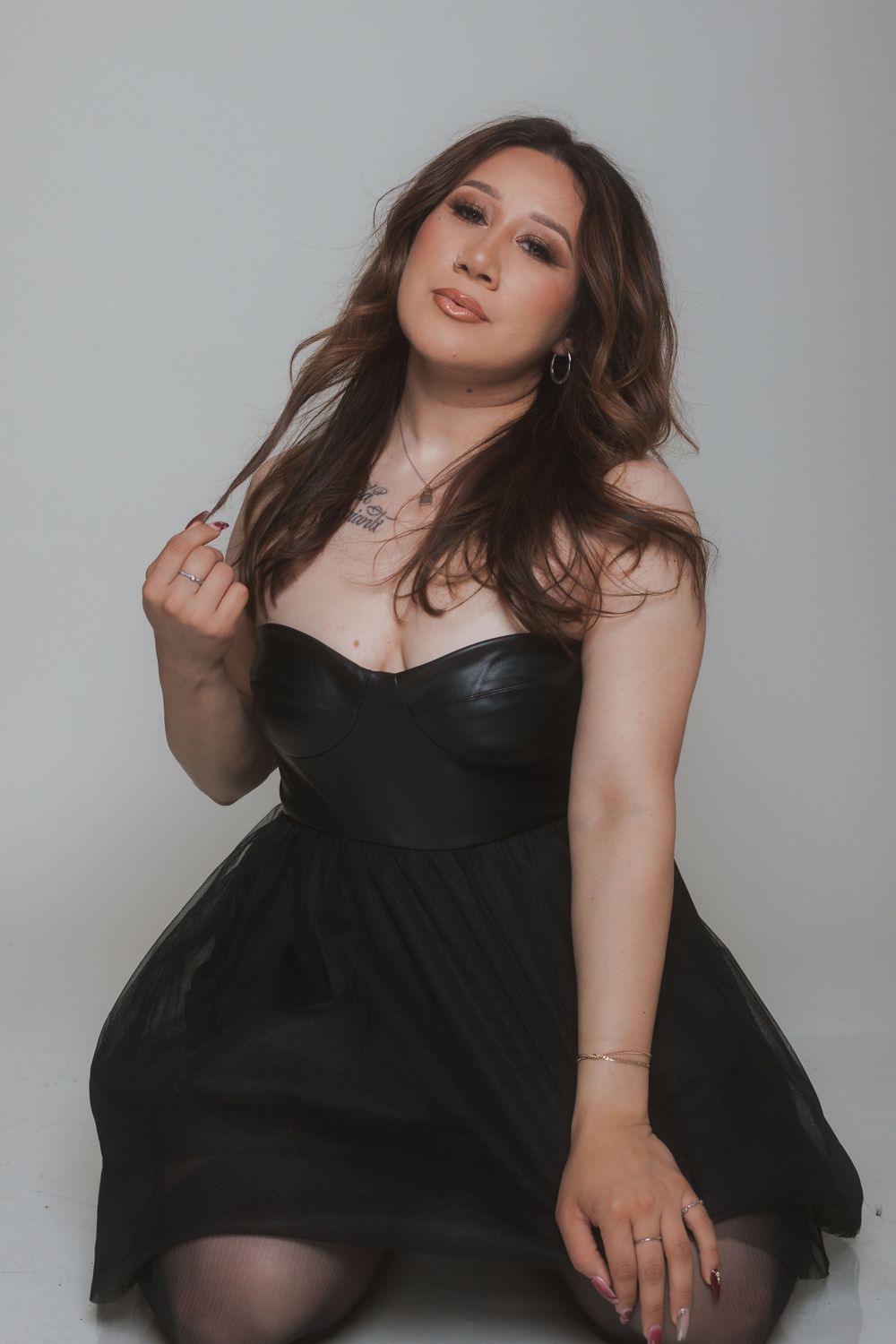 A glamour portrait featuring a black cocktail dress and tousled waves against a neutral backdrop.