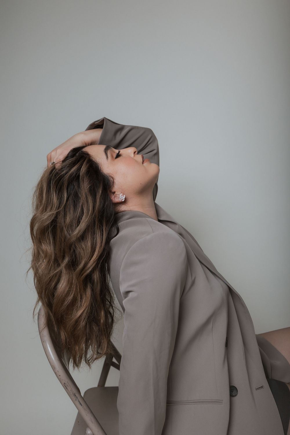 Dramatic portrait in a taupe blazer with flowing hair against grey background.