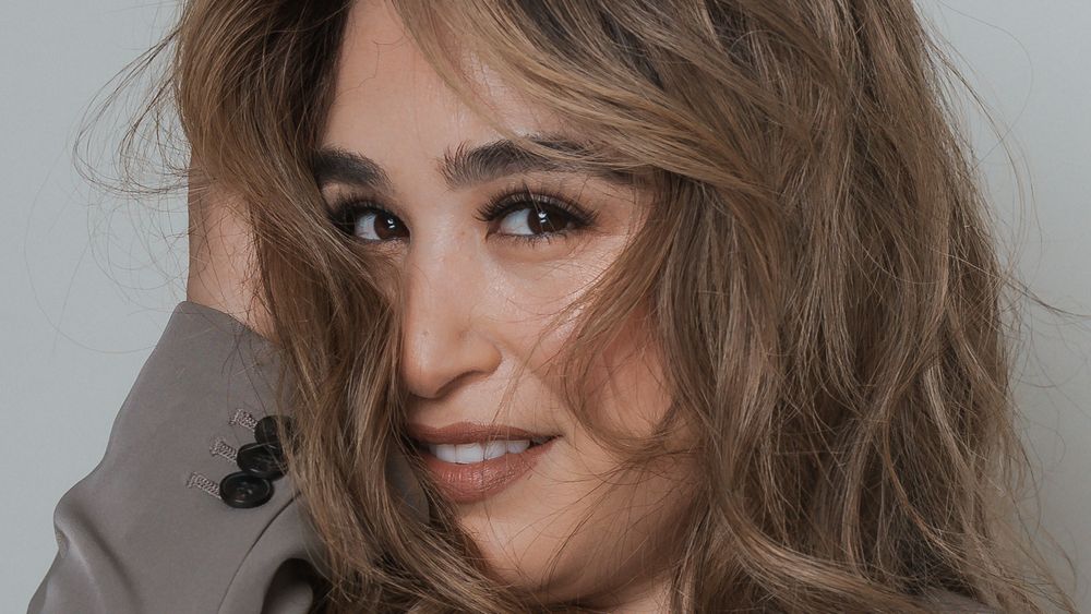 Close-up beauty portrait with windswept hair against grey background.
