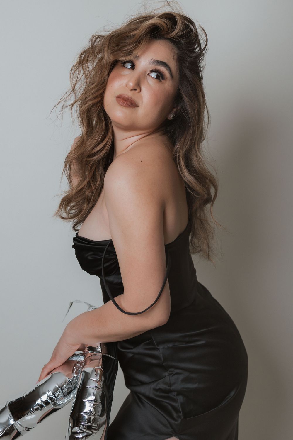 Fashion portrait in black dress with metallic boots against grey wall.
