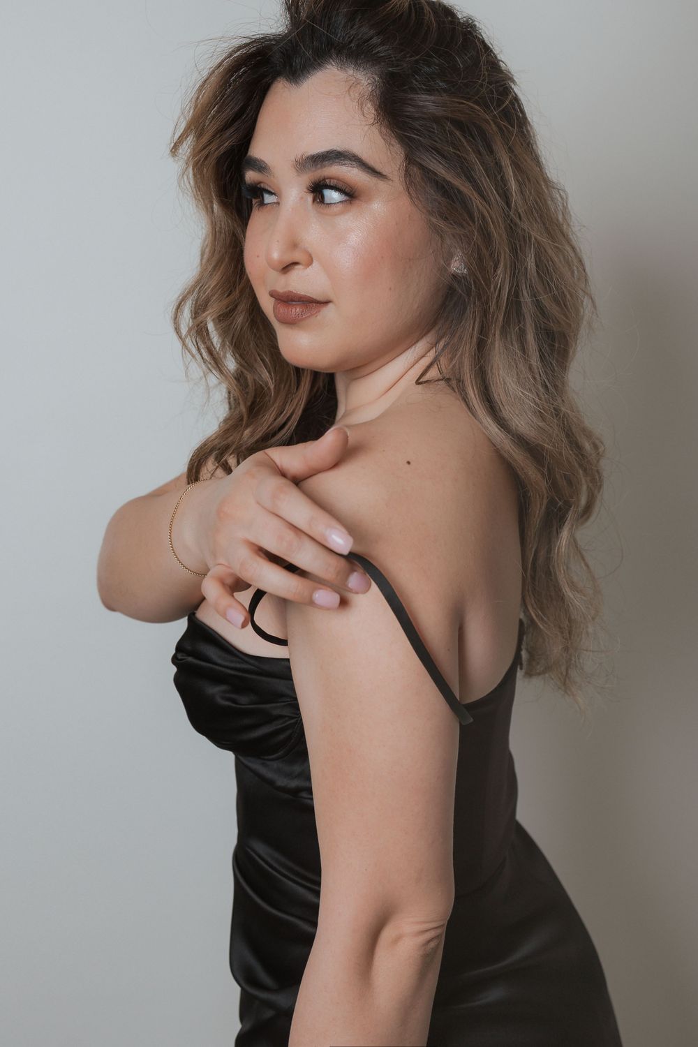 Stylish portrait of a woman in a black velvet dress posing with wavy hair against a light gray background.