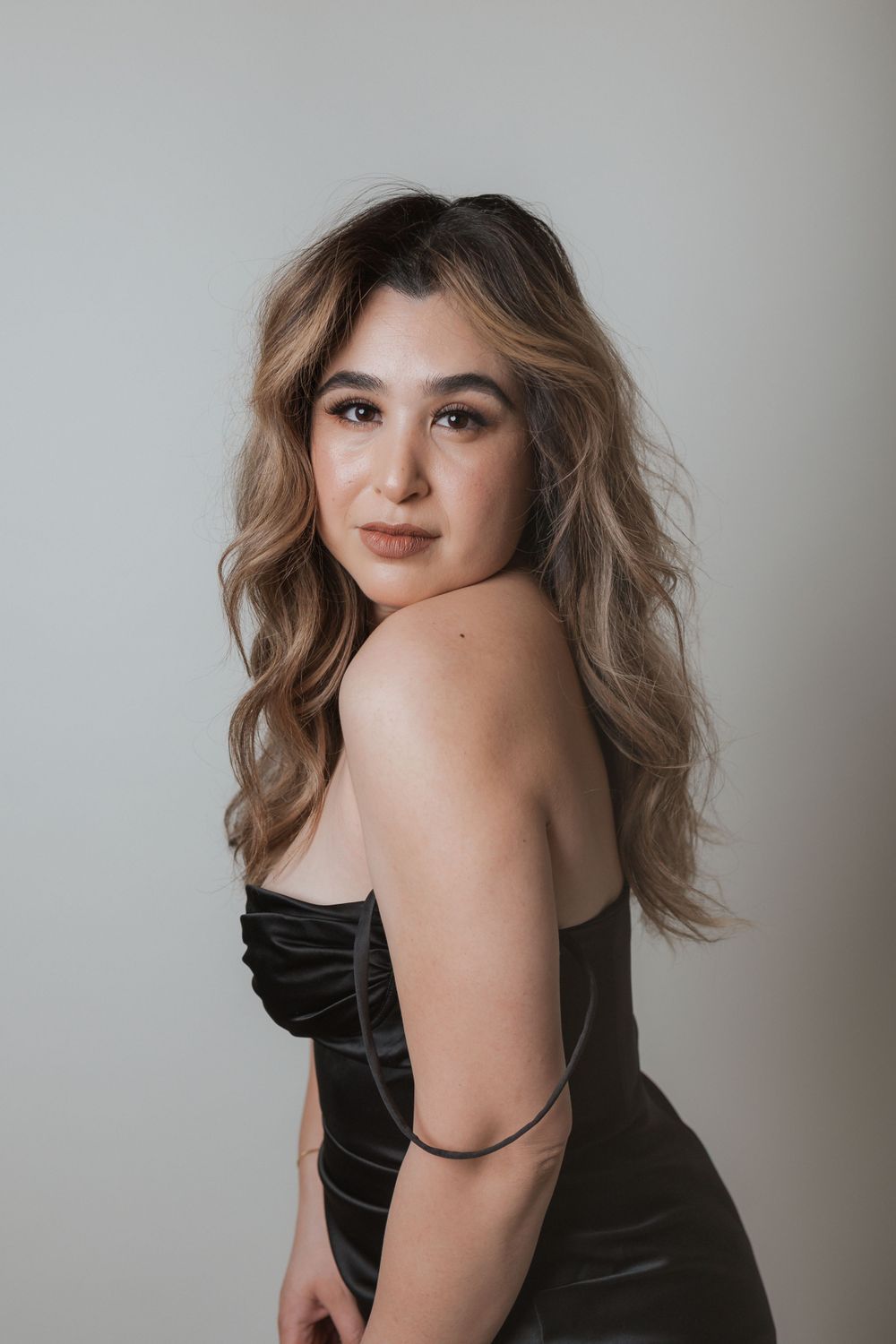 Side profile portrait of a woman in black strapless dress with highlighted caramel waves.