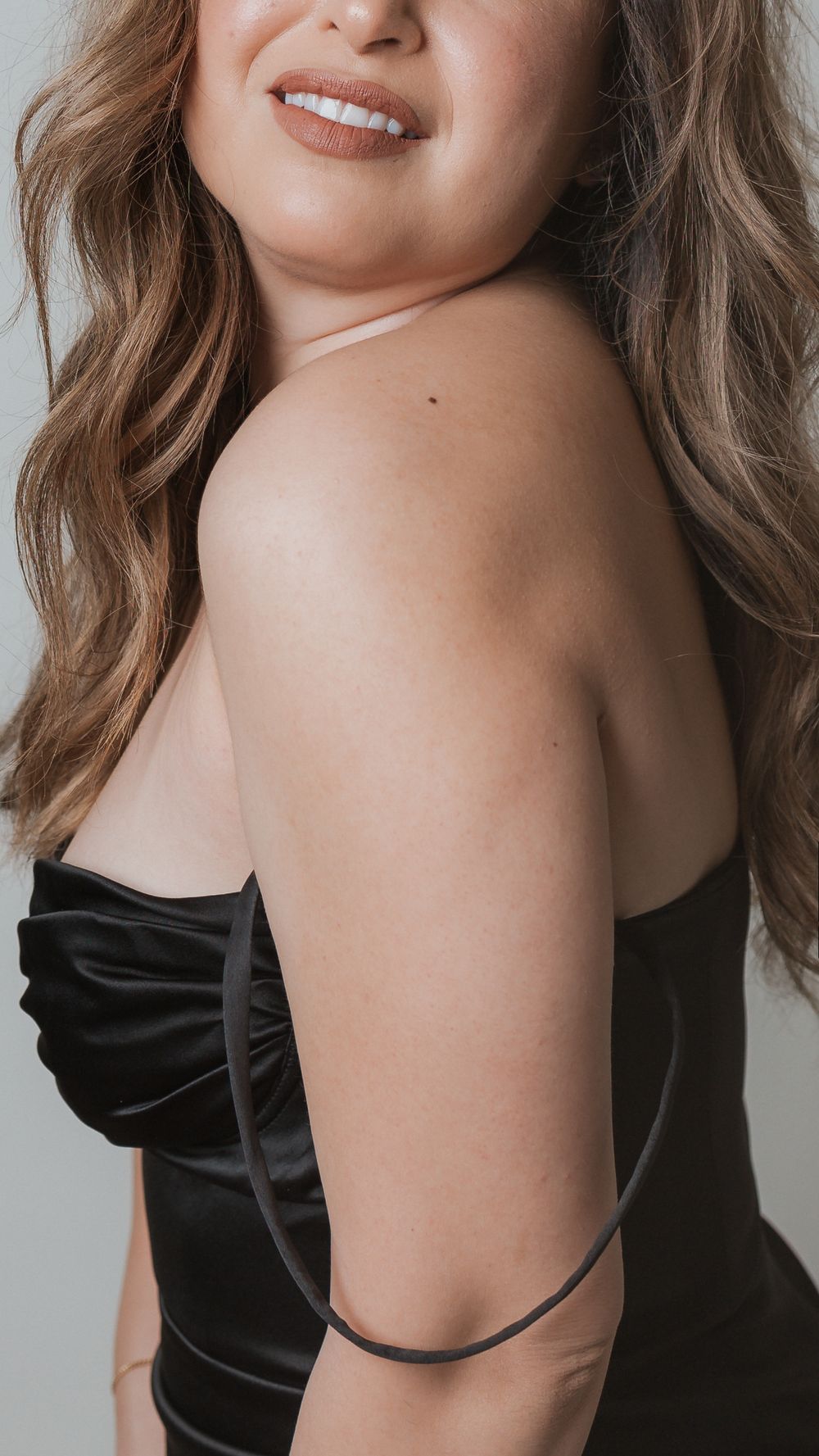 Close up shot showing woman's shoulder and smile while wearing black strapless dress.
