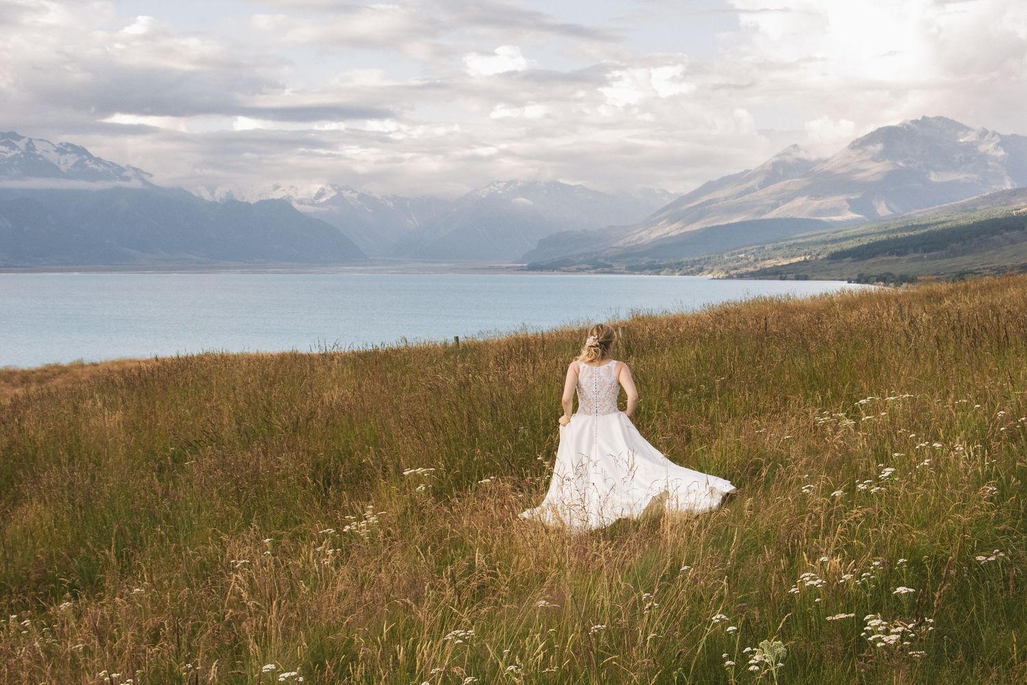 A flowing white wedding dress twirls against a stunning mountain lake backdrop.