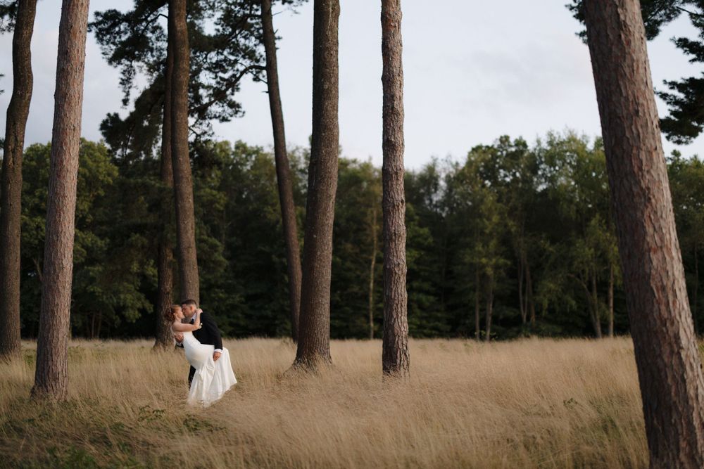 A couple dances in a field surrounded by tall pine trees.