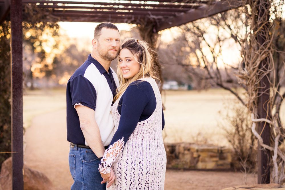 A couple wearing coordinated navy and white outfits embraces under a wooden pergola at sunset.