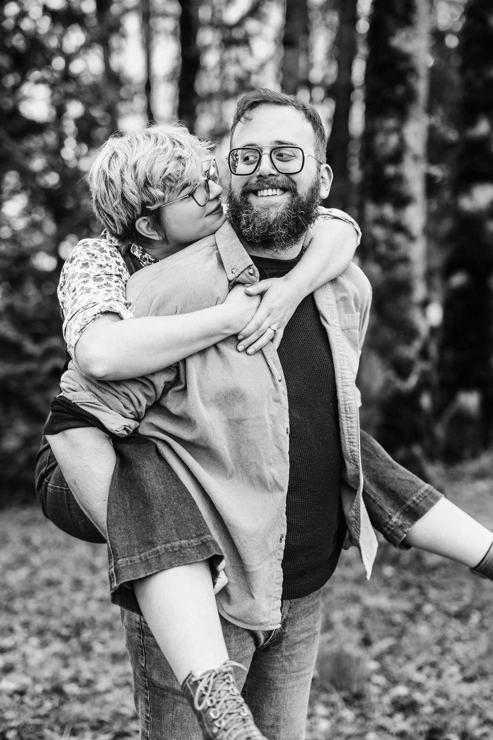 A joyful black and white portrait of a bearded man giving a playful piggyback ride in a forest setting.