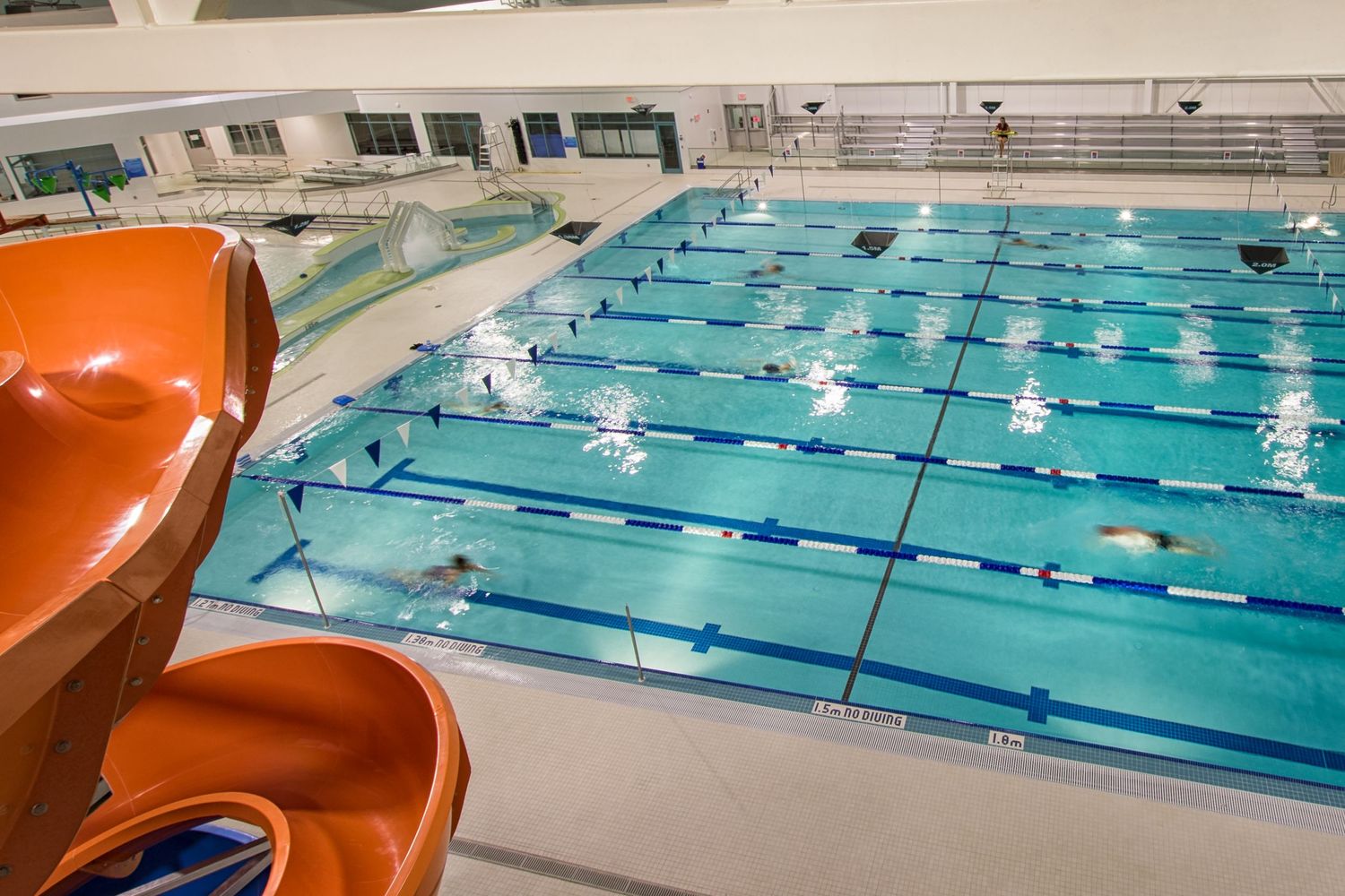 Indoor Olympic swimming pool with lap lanes and orange water slide in foreground.