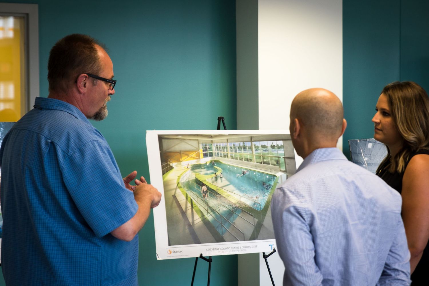 Three people reviewing architectural rendering of an indoor swimming pool on an easel.