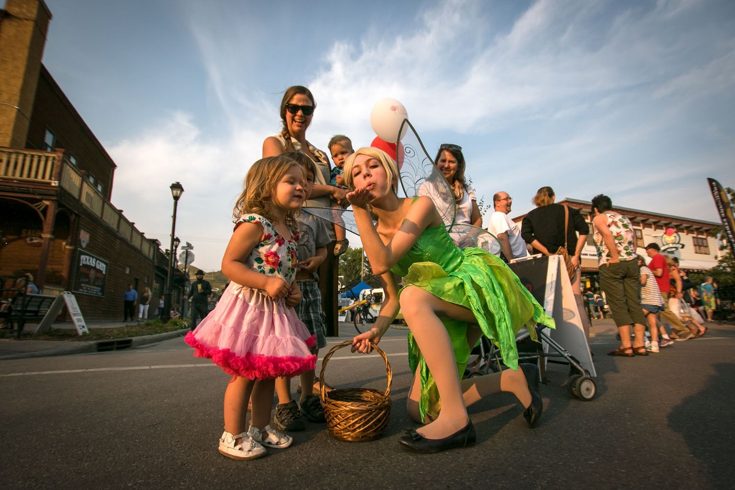 Child in pink dress meeting Tinker Bell character during outdoor street festival parade.