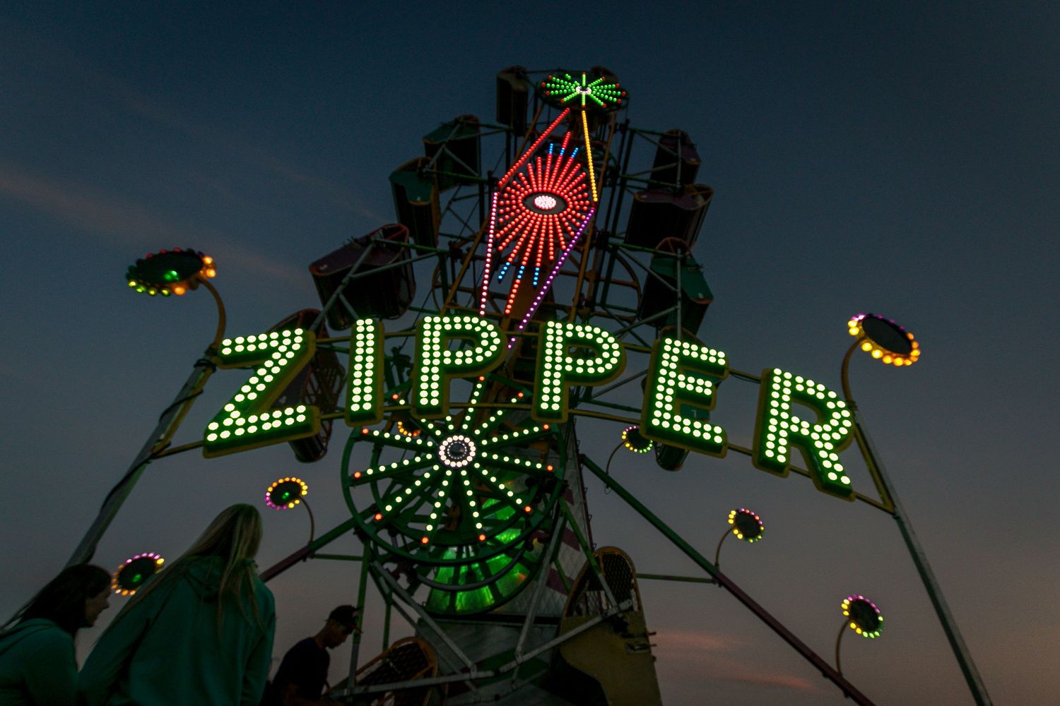 Colorful illuminated Zipper carnival ride sign glowing at dusk at outdoor fairground.