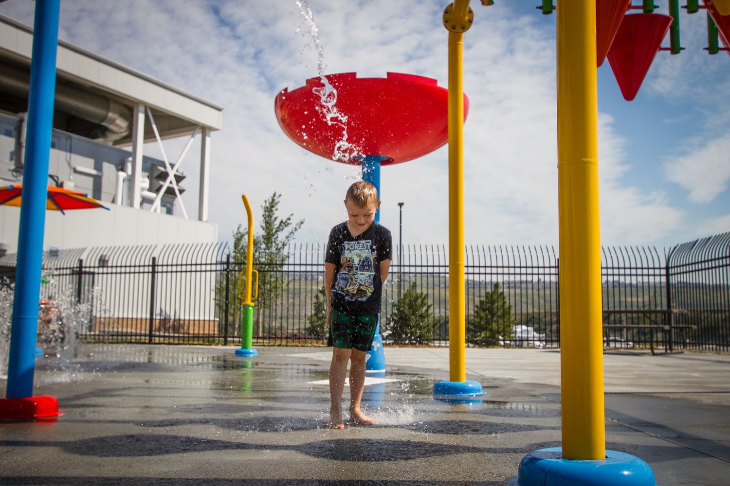 Young boy playing at colorful outdoor splash pad water park on a sunny day.