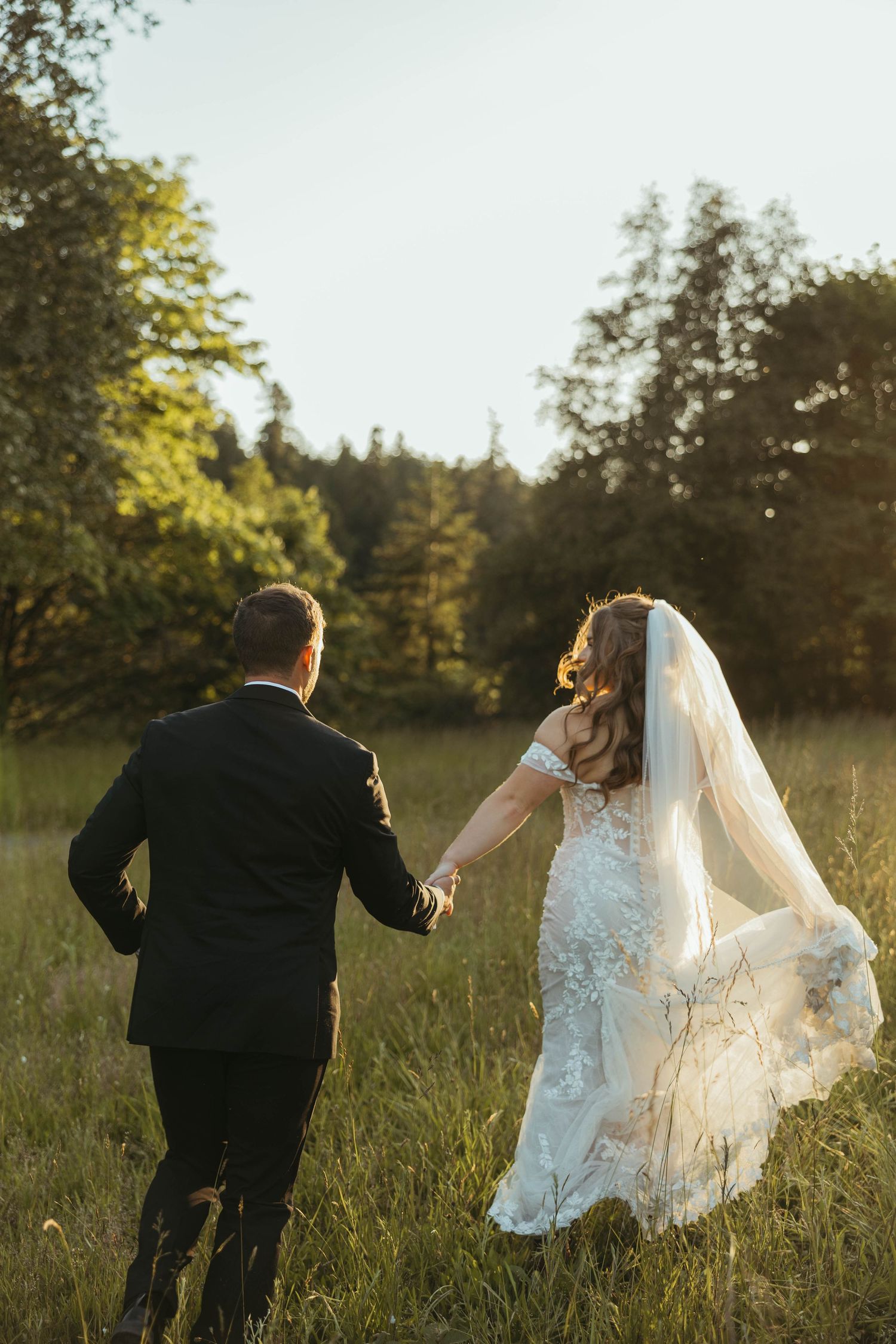 Newlyweds running through a sunlit meadow with flowing wedding dress and veil.