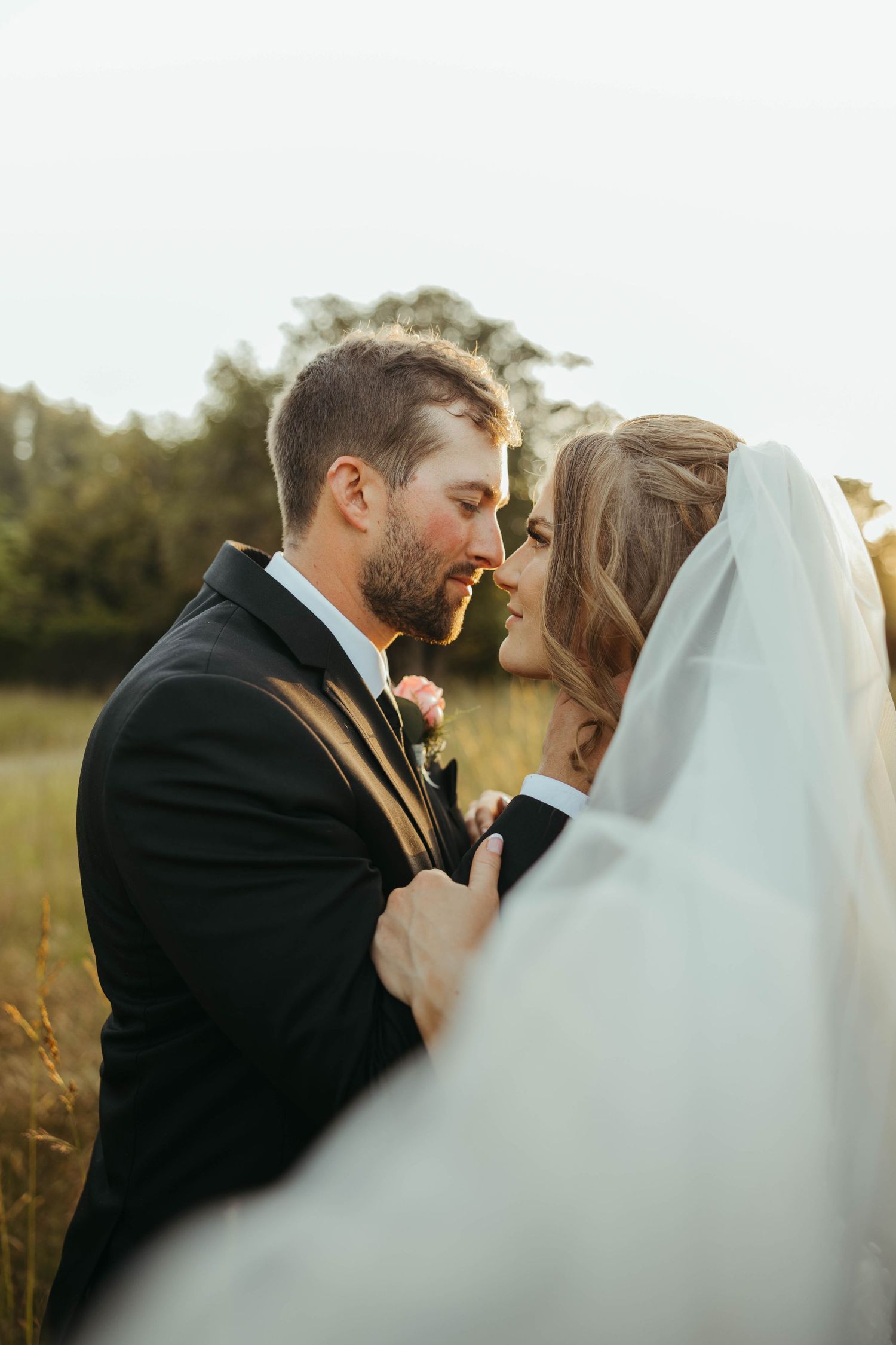 Romantic wedding couple embracing in golden hour light with flowing white veil.