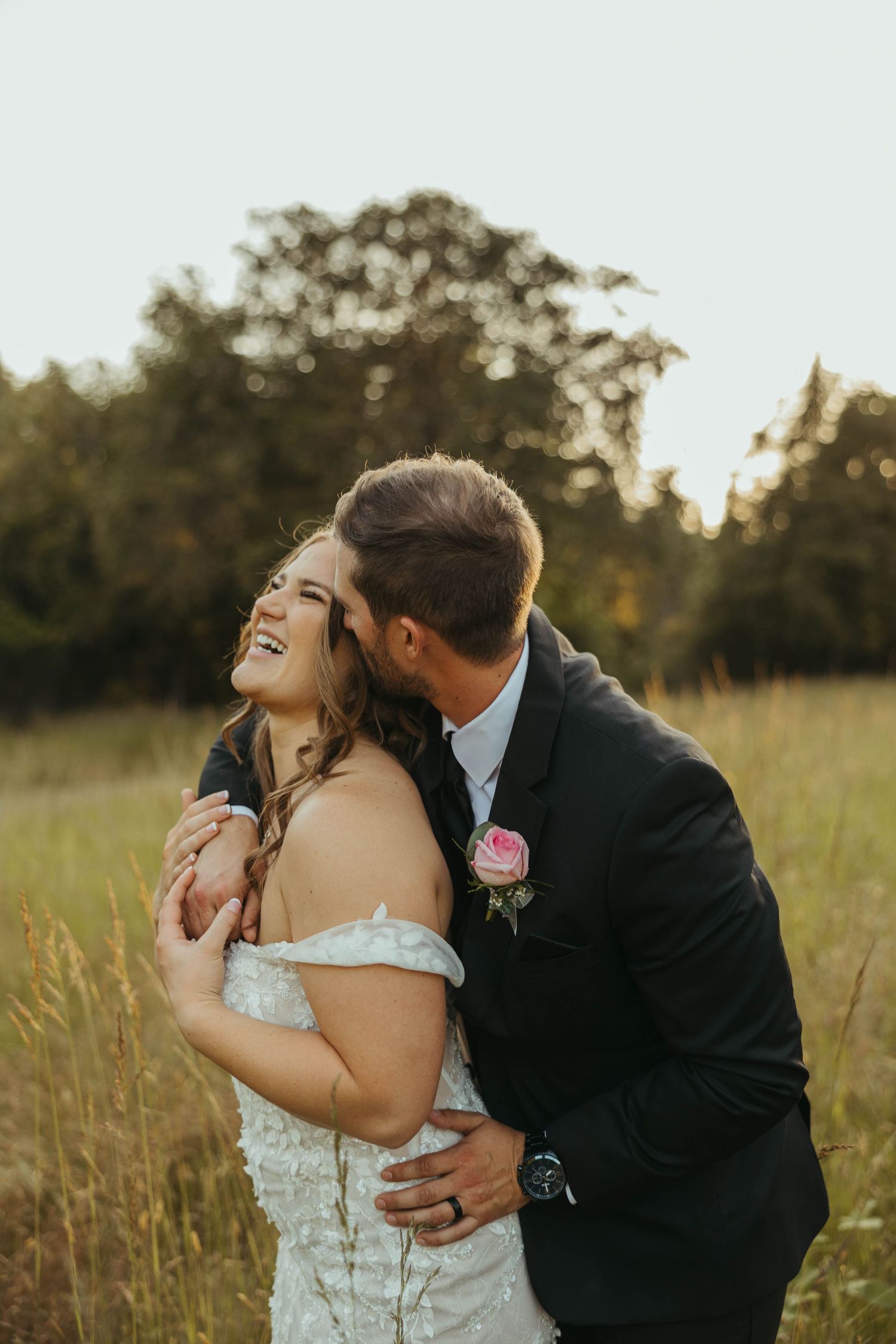 Wedding couple sharing joyful laughter during sunset portrait session in field.