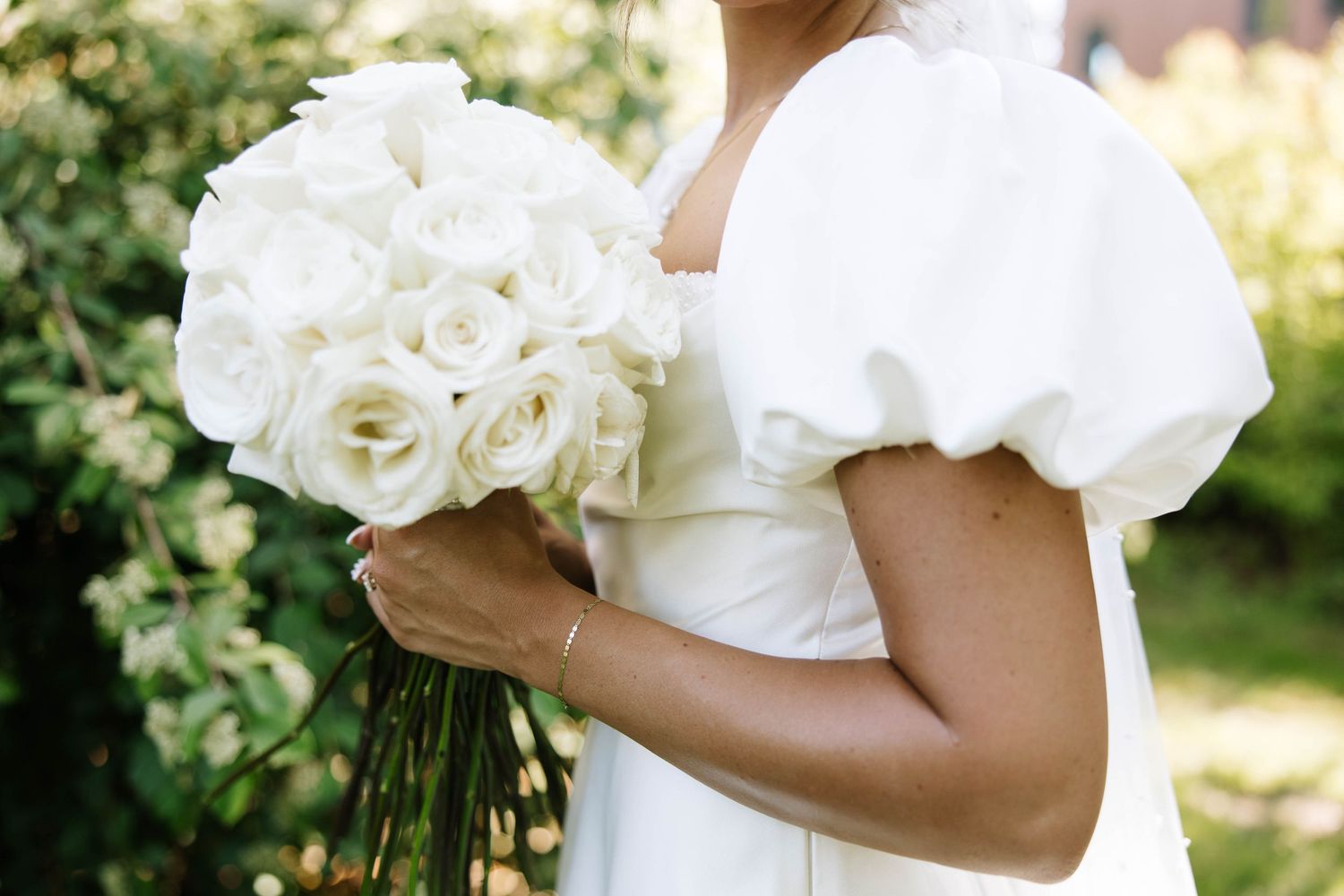 Close-up details of white wedding dress and bouquet in natural outdoor lighting.