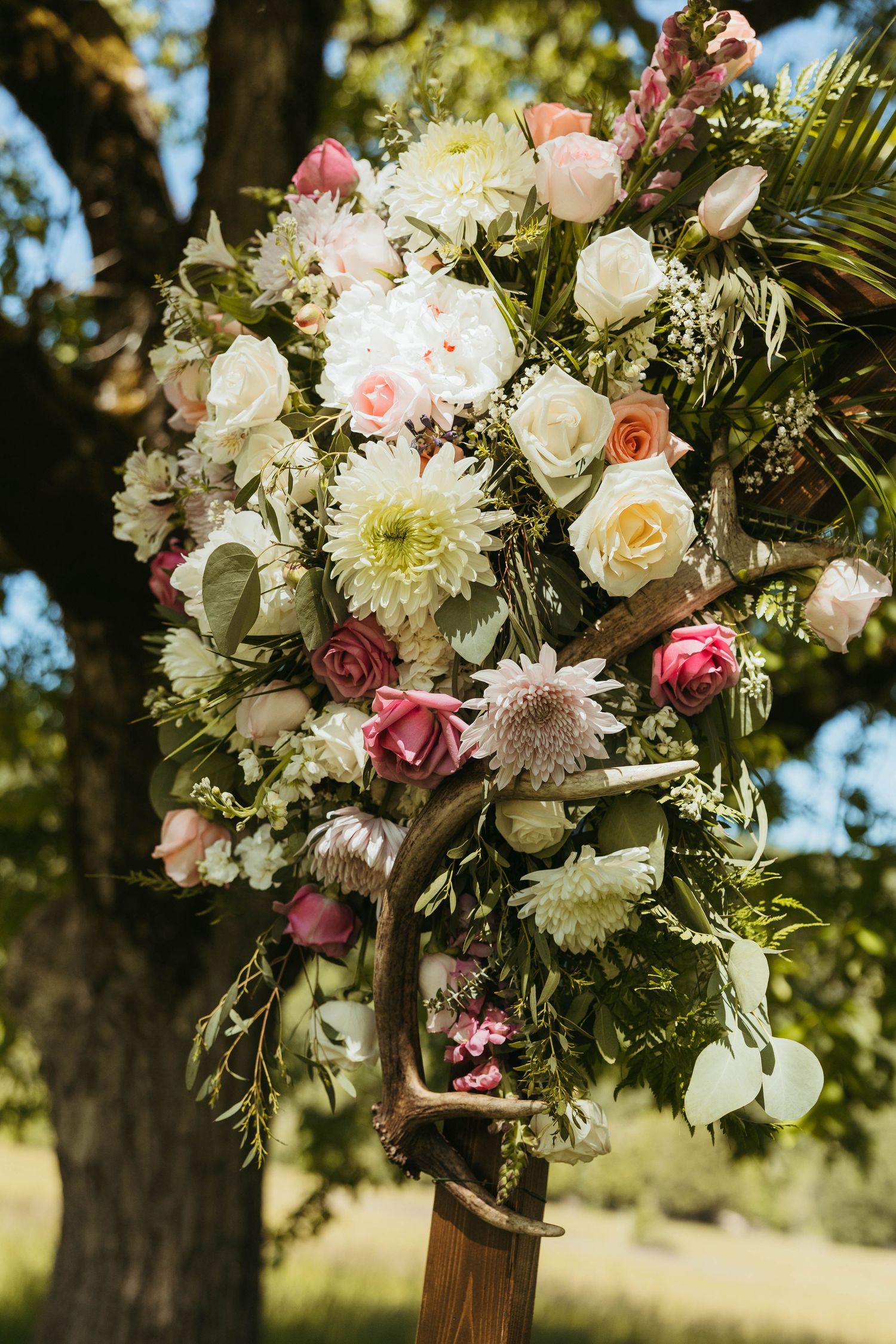Elegant floral arrangement with white and pink roses decorates an outdoor wedding arch.