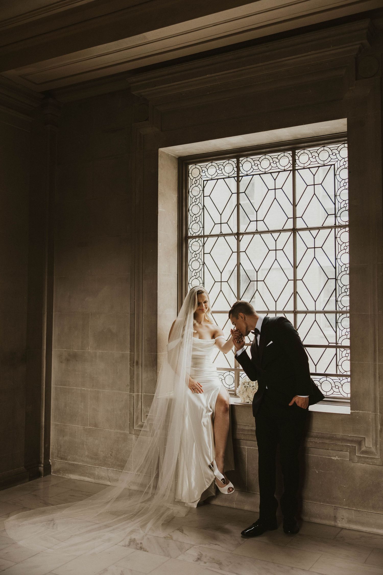 Wedding couple dancing by geometric window in dramatic black and white.