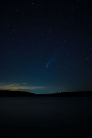 Bright comet streaks across dark night sky over a serene lake landscape.
