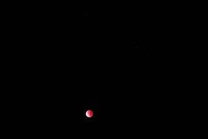 Blood moon glows red against black night sky during lunar eclipse.