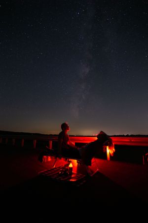 Silhouettes of stargazers with red lighting under the Milky Way at night.