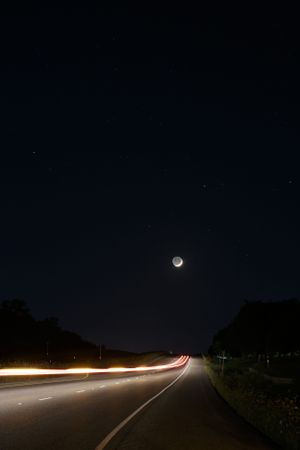 Full moon illuminating a dark highway with car light trails.