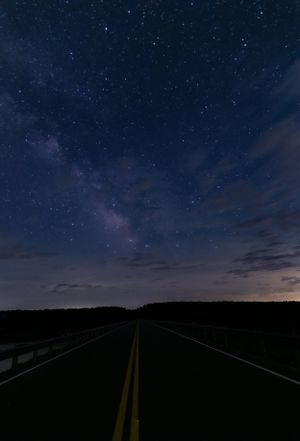 Starry night sky with Milky Way visible above an empty rural road.