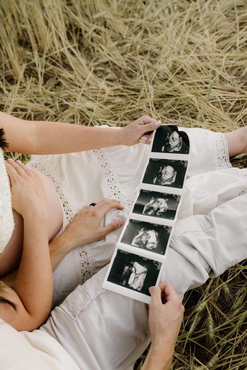 Hands holding ultrasound photos while lying in dried grass.