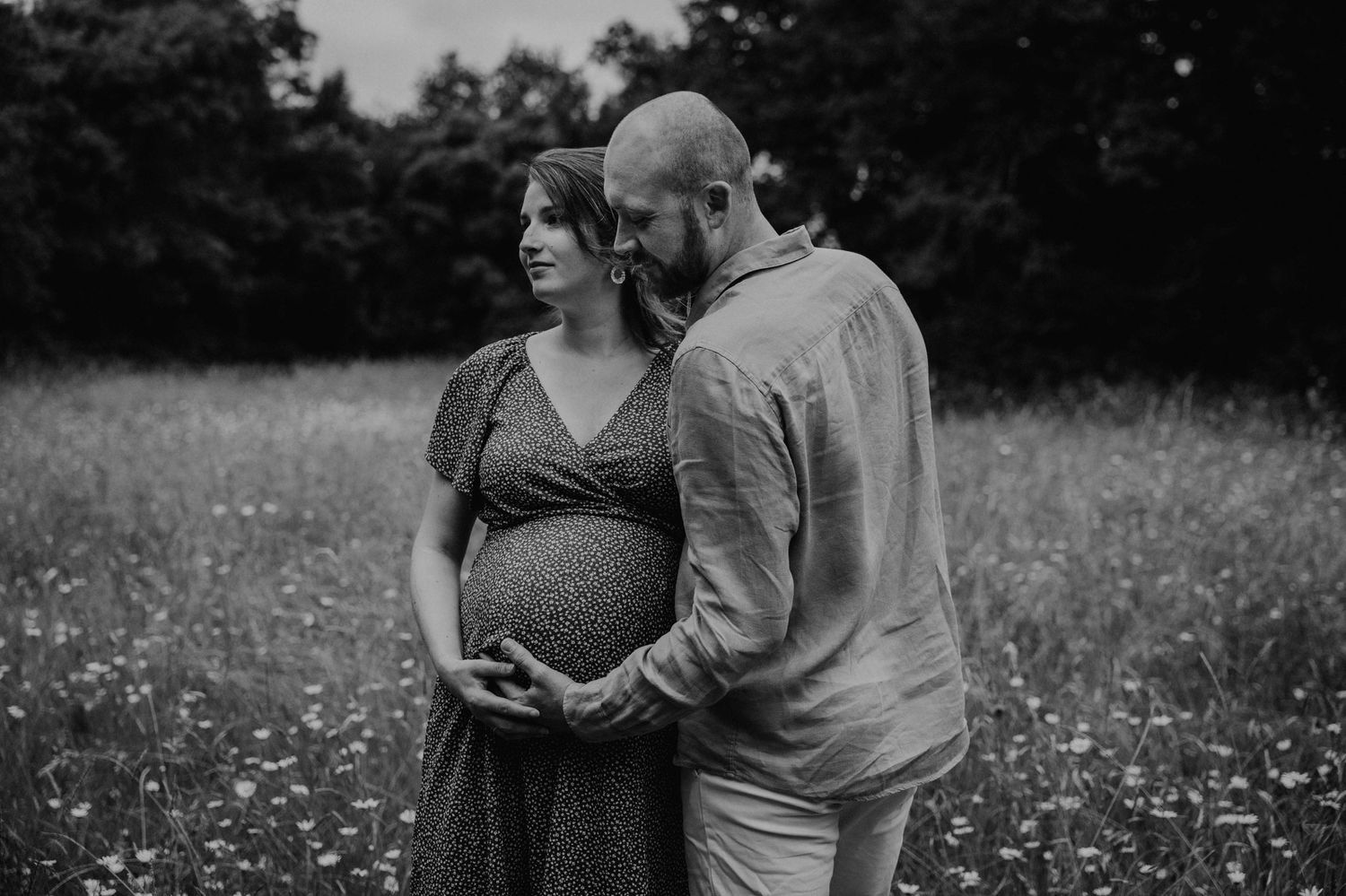 A couple embraces tenderly in a sunlit meadow filled with wildflowers during a romantic outdoor photoshoot.