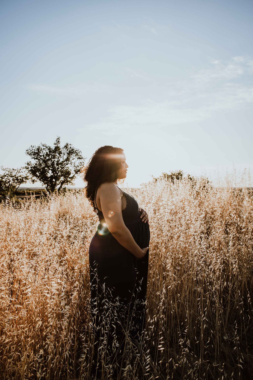 Silhouetted figure stands in golden wheat field at sunset with warm backlight creating dramatic contrast.