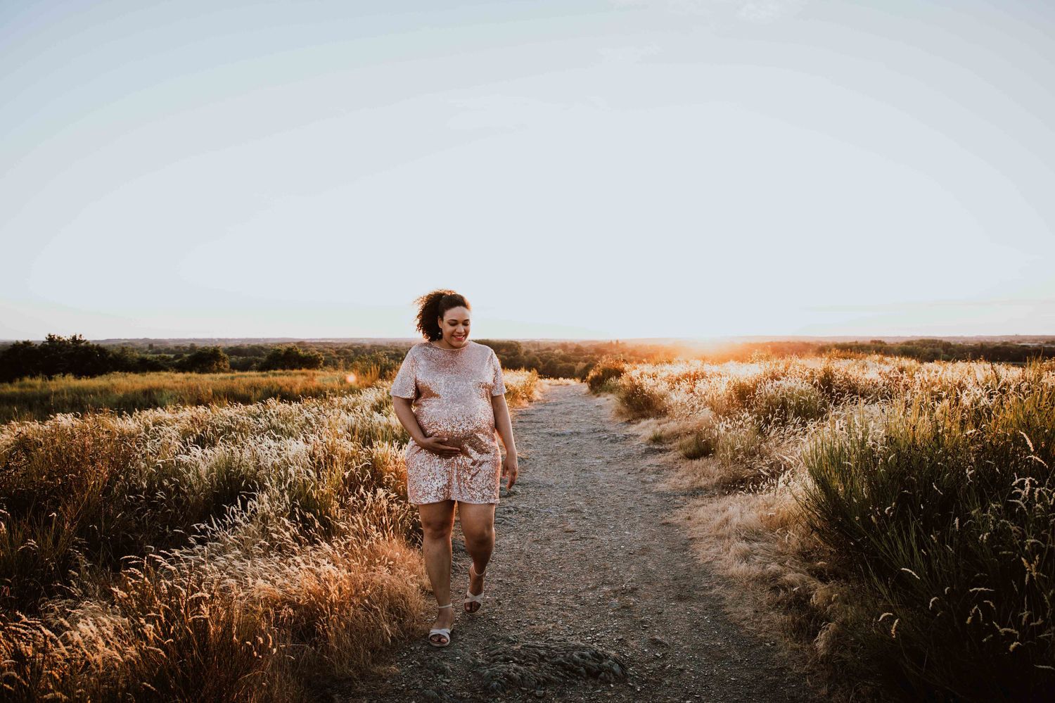 A person walks along a dirt path through golden grass at sunset, creating a serene outdoor scene.