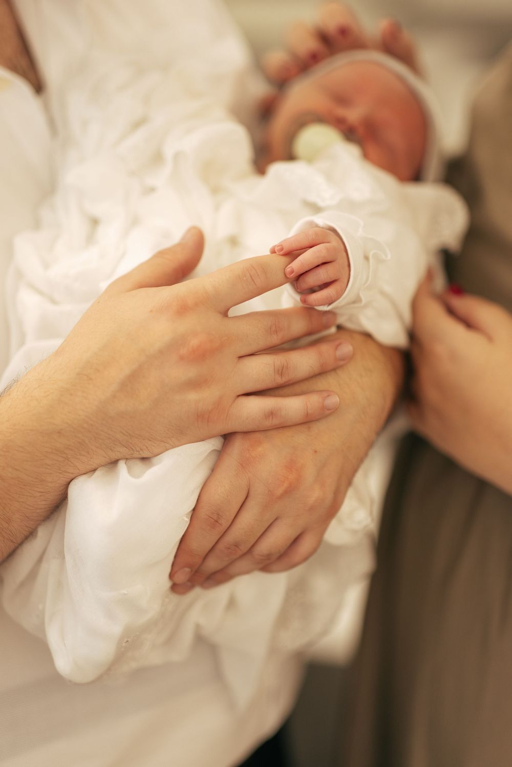 Tender moment of hands holding a newborn baby wrapped in white cloth.