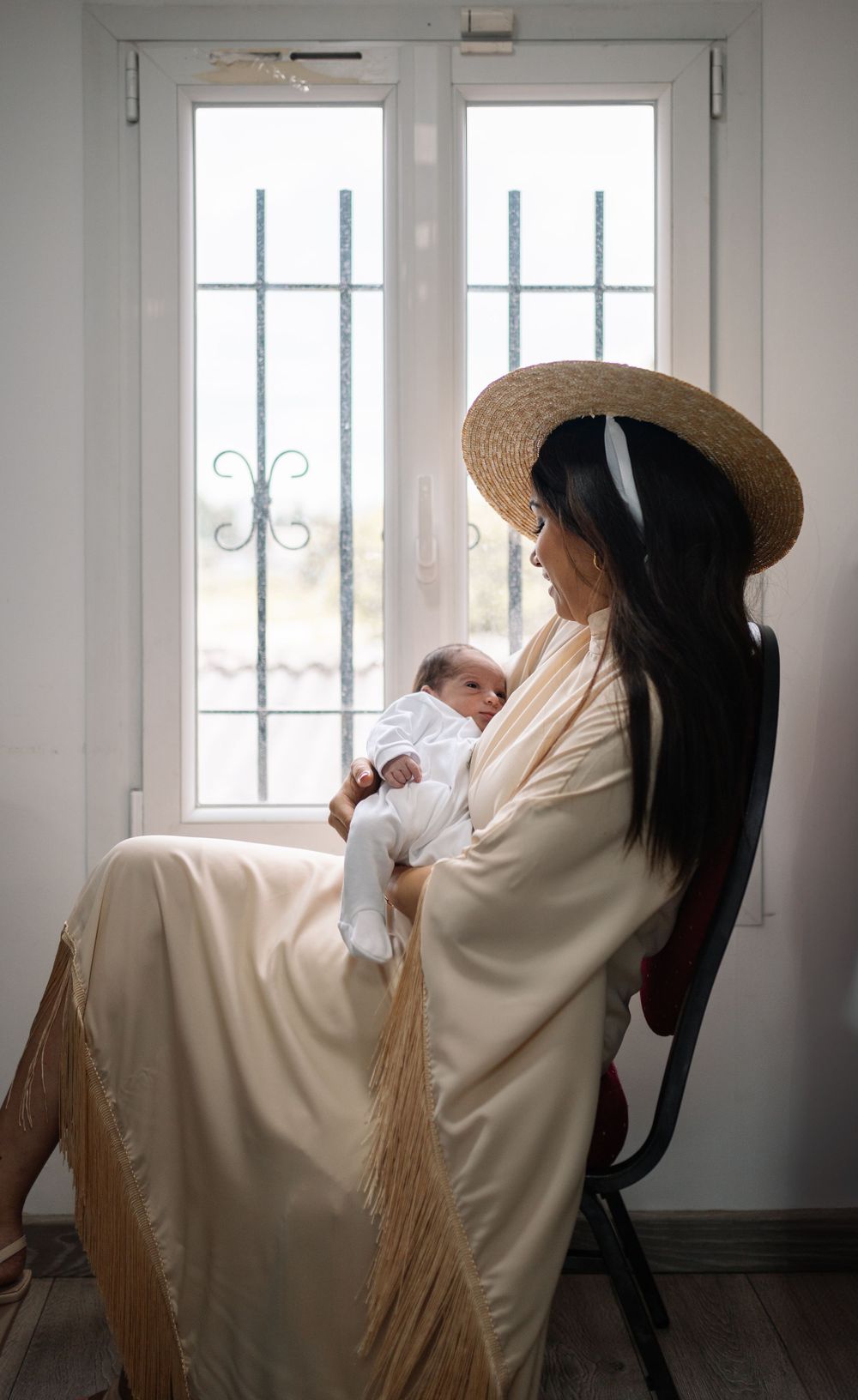 A peaceful nursery scene by a window with natural light illuminating a mother and baby in white.