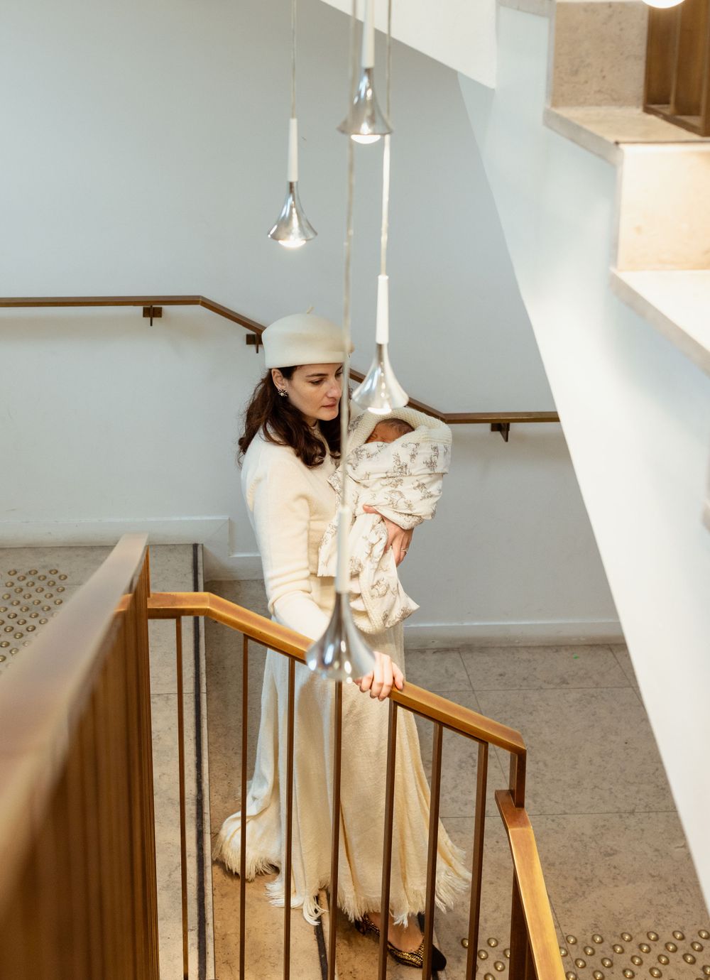 A touching moment on a staircase as a white-clad figure holds a bundled infant.
